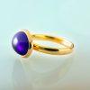 Oval amethyst cabochon (4.46ct) set in 18ct yellow gold. Side profile on green background.