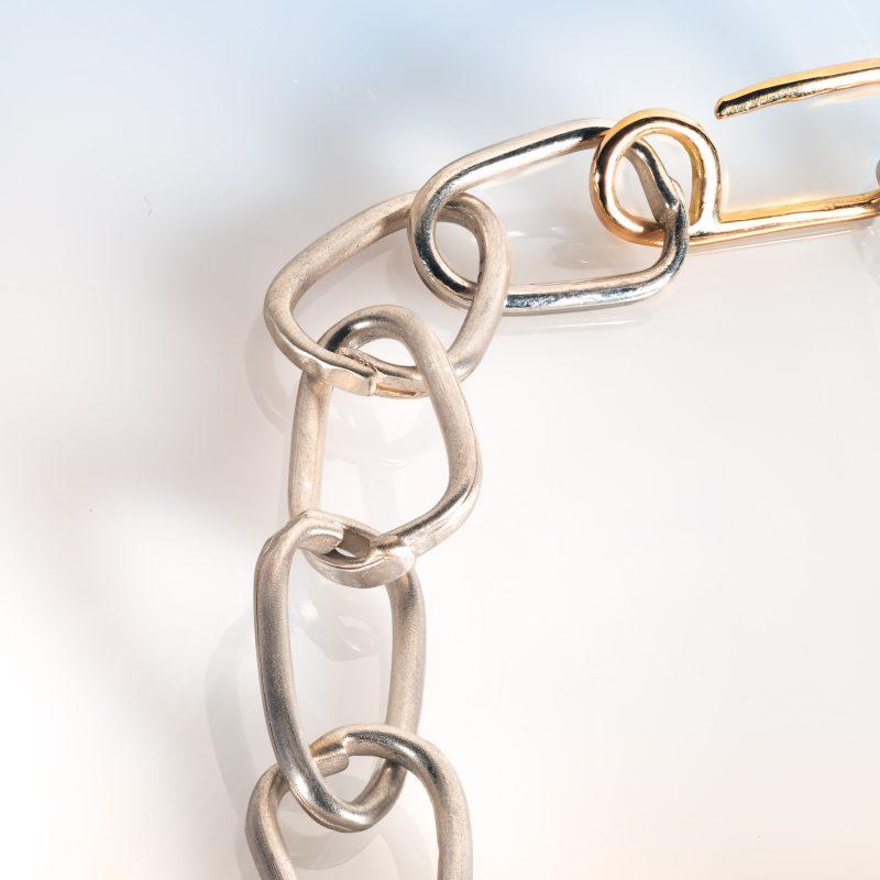 close up of Cox & Power Force of Nature Silver Link Bracelet, showing details of silver links and handmade 18ct gold clasp. Shown on gradient background from pale blue to pale orange.