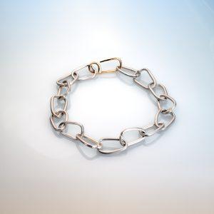 Cox & Power Force of Nature Silver link bracelet: interlocking free-form links with 18ct gold handmade clasp. Shown against a soft gradient background, from pale blue to pale orange.