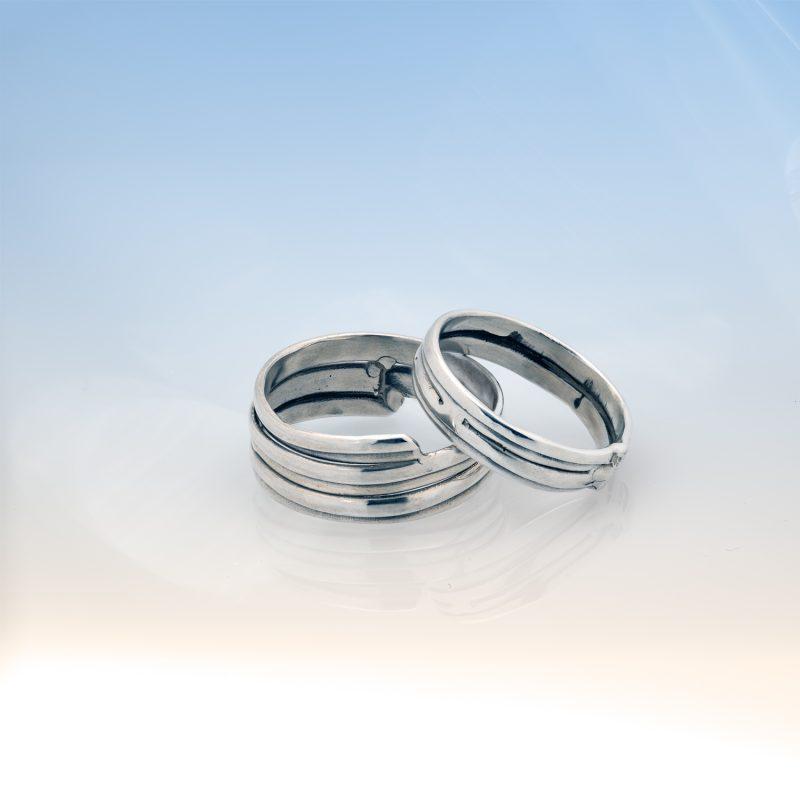Two sterling silver rings from Force of Nature Collection - wider band and narrower band with parallel layered grooved patterns against soft blue background.