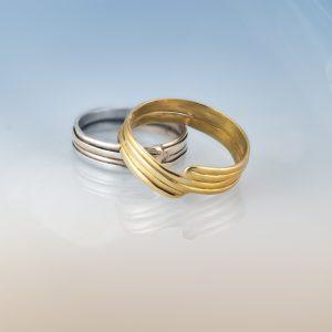 Close-up of two handcrafted wide wrapped band rings from the Force of Nature collection, one in polished sterling silver and the other in 18ct Fairmined gold, displayed on a soft gradient background.