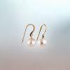 Pair of white pearl drop earrings with 18ct rose Fairmined gold hooks against a soft gradient background