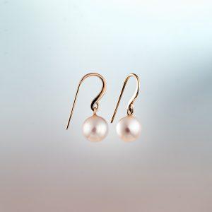 Pair of white pearl drop earrings with 18ct rose Fairmined gold hooks against a soft gradient background