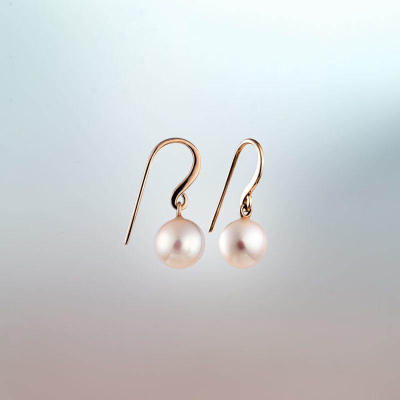 Pair of white pearl drop earrings with 18ct rose Fairmined gold hooks against a soft gradient background
