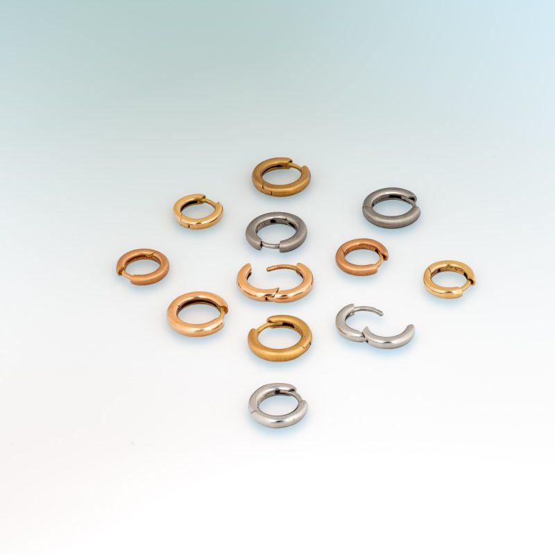 Group shot of small hinged hoop earrings in platinum, 18ct yellow gold, and 18ct rose gold, arranged on a soft gradient background and showing earring posts.