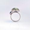 Underside ide view of a platinum Ribbon ring with a wide, tiered band, showing the domed cabochon moonstone rising above the setting, with an orange pear-shaped rose-cut diamond and a green cabochon tourmaline shown off-set to the left side of the moonstone.